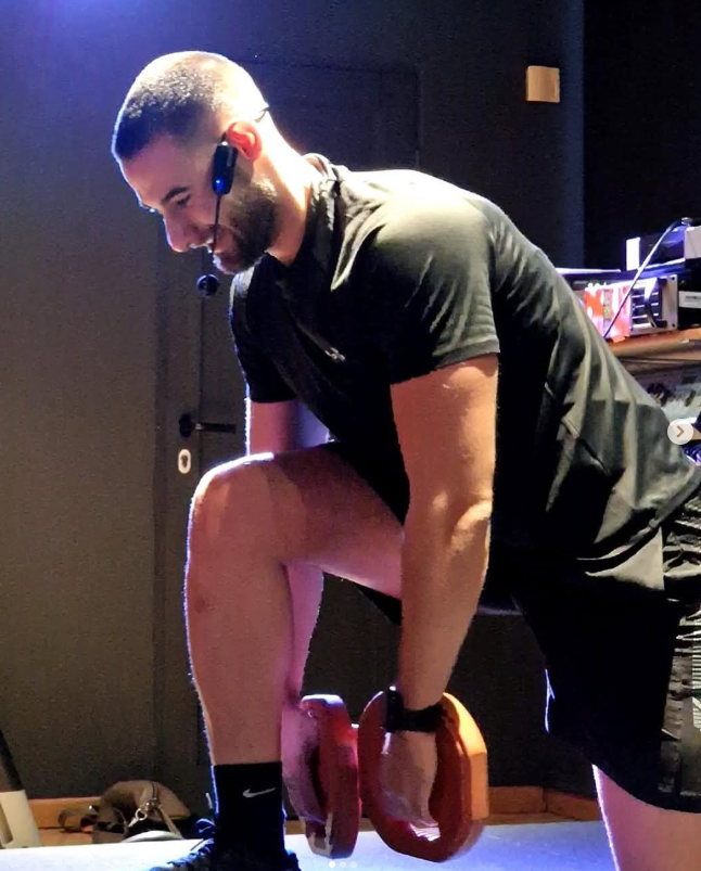 Photo of the personal trainer Apostolis Kontotasios doing a barbel squat with microphoen in front of the audience